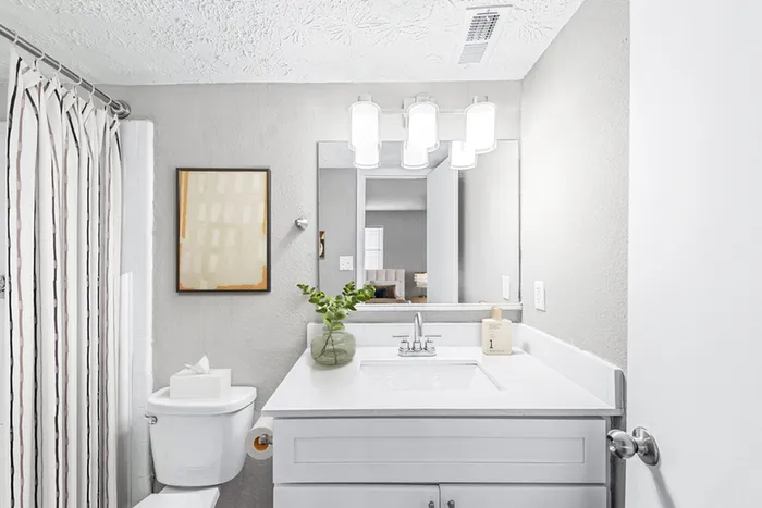Bathroom with quartz counters, large mirror, vanity lighting, and white cabinetry