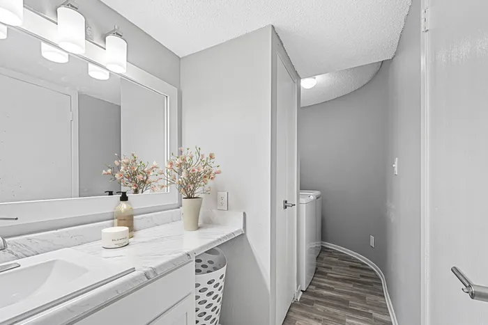 Bathroom with quartz counters, large mirror, vanity lighting, and white cabinetry