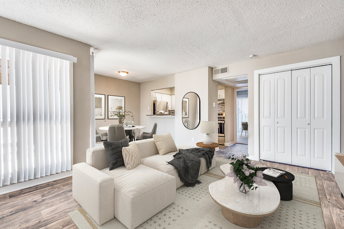 Living room, beige couch with pillows, white coffee table, double closet doors, wall art, hard wood style flooring with rug