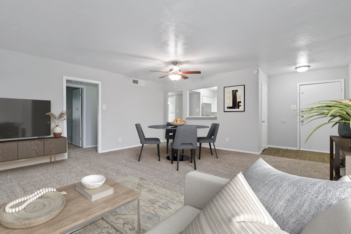 Carpeted living space, wooded coffee table and entertainment center, ceiling fan light fixture, beige couch throw pillows