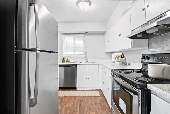 Renovated kitchen stainless-steel refrigerator, oven, and dishwasher, sleek white cabinets, gray subway tile backsplash, and wood flooring
