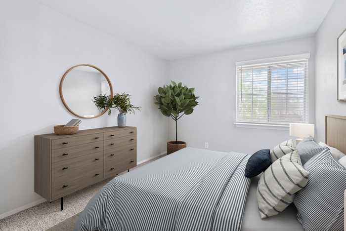 Carpeted bedroom, blue bedding, wooden dresser, circular wall mirror