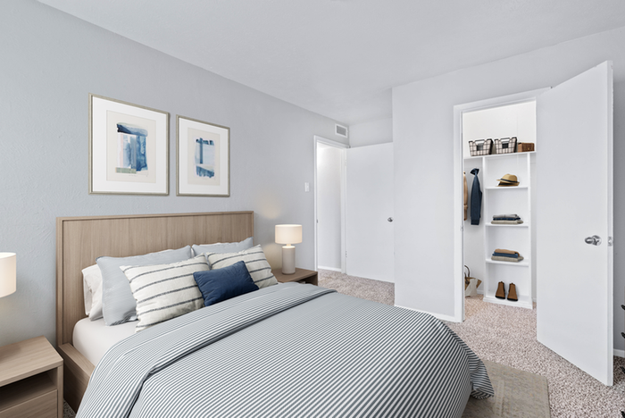 Carpeted bedroom, queen-size bed with blue striped bedding, wall art, wooden end table, table lamp