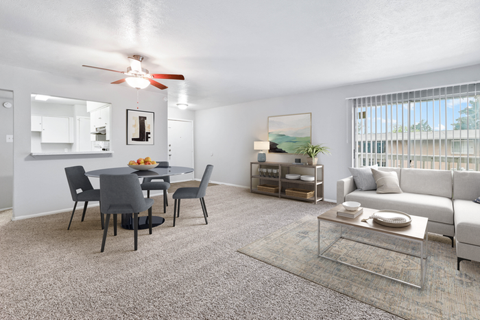 carpeted living room, rug, round gray dining chair, wooded coffee table, white sectional, large glass sliding patio doors, ceiling fan light fixture