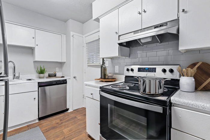 Renovated kitchen stainless-steel oven, and dishwasher, sleek white cabinetry, gray subway tile backsplash, and wood flooring