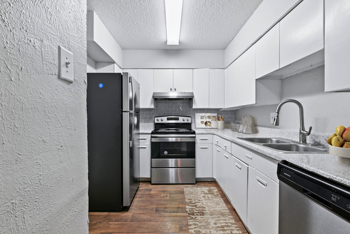 Renovated kitchen stainless-steel refrigerator, oven, and dishwasher, sleek white cabinets, gray subway tile backsplash, and wood flooring