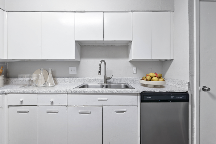 Renovated kitchen with sleek white cabinetry, stainless steel dishwasher, and sink with gooseneck faucet