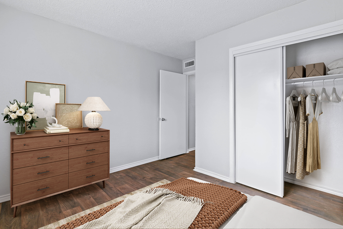 bedroom, hard wood floors, wooden dresser, table lamp, open sliding closet, bedding, rug