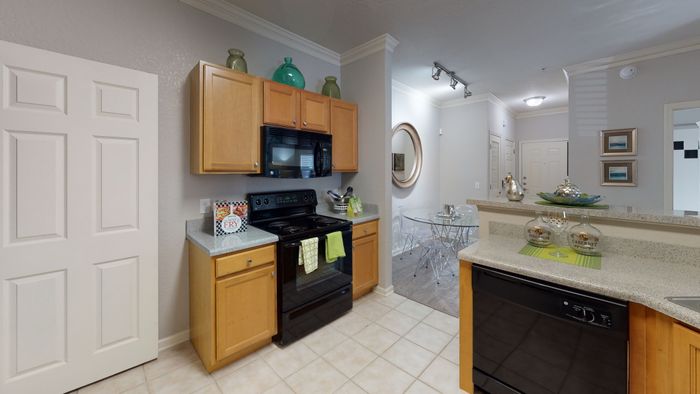 staged model of kitchen with wood cabinets, granite style counters, and black appliances