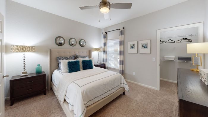 staged model of bedroom with beige carpe, large bed and ceiling fan