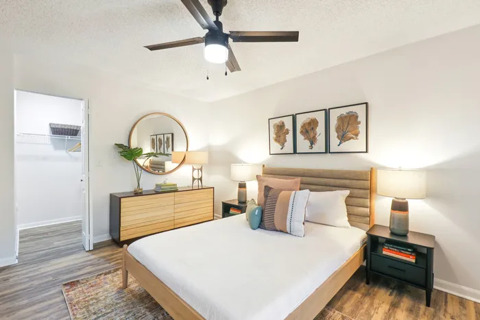 Bedroom with queen size bed and wooded framing, hard wood style flooring, ceiling fan light fixture, copen closet door, wooded dresser, circular mirror