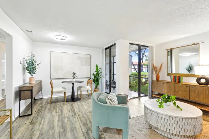 Living room blue cushioned chair, hardwood style flooring, wooded dresser, floor to ceiling glass patio doors