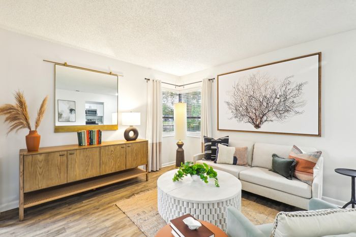 Living room, circular coffee table, brown  table, white couch, adjacent windows, wall art