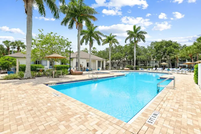 Pool with sun deck blue lounge chairs, exterior building, palm trees and native landscaping