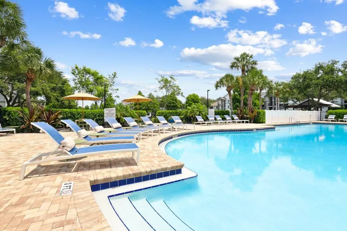 Pool with sun deck blue lounge chairs, exterior building, palm trees and native landscaping