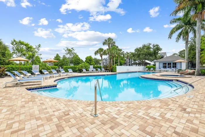 Pool with sun deck blue lounge chairs and tan umbrellas, exterior building, palm trees and native landscaping