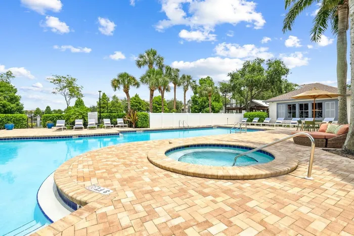 Pool with sun deck blue lounge chairs, exterior building, palm trees and native landscaping and circular mini-pool