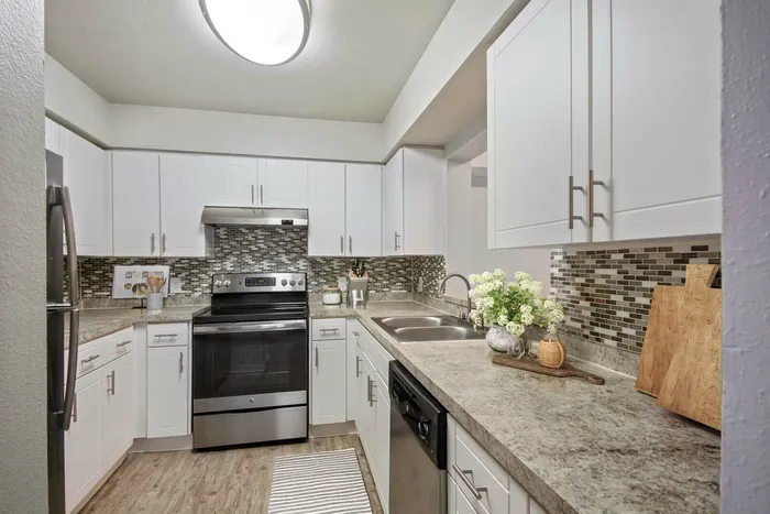 Kitchen with hardwood flooring, stainless steel appliances, white cabinetry, black and tan mosaic backsplash