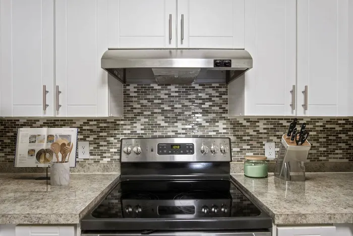 White cabinetry, stainless steel stove and oven, tan and black mosaic backsplash, tan granite counters