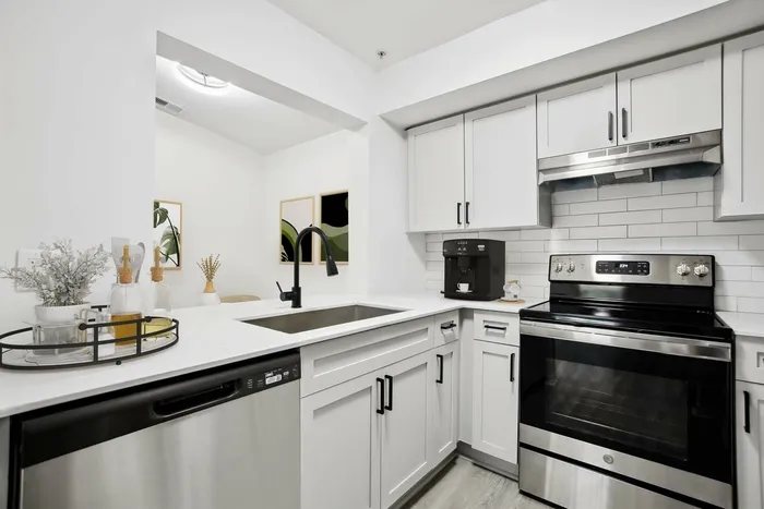 Kitchen with white quartz counters, stainless steel appliances, white subway tile backsplash, undermount sink with gooseneck faucet, hardwood style flooring