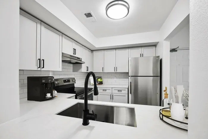 Kitchen with white quartz counters, stainless steel appliances, white subway tile backsplash, undermount sink with gooseneck faucet, hardwood style flooring