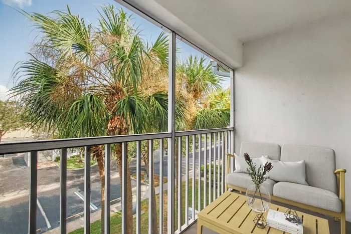 Screened in patio, gray storage door, palm trees and parking lot, wooden patio table, gray patio lounge