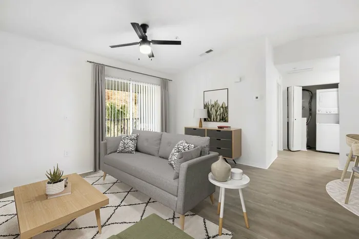 Living room with gray couch, rug on hard wood style flooring, ceiling fan light fixture, wooden coffee table, glass patio doors