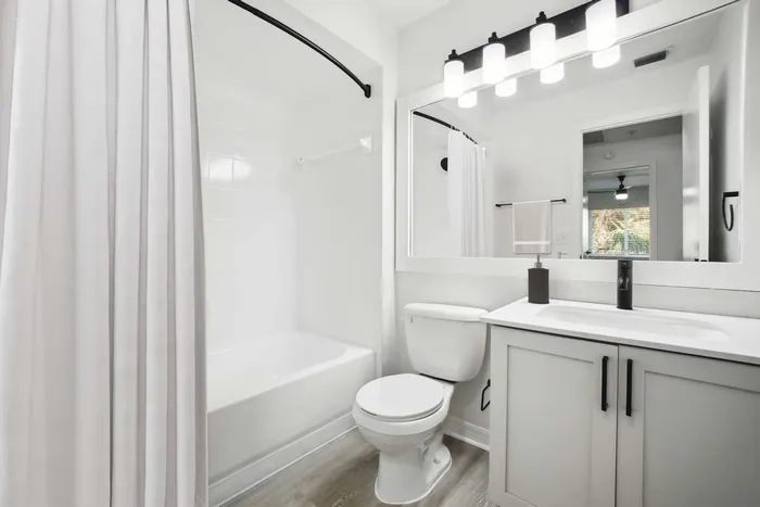 bathroom with large vanity mirror and lighting, curved shower rod, quartz counters and white cabinetry