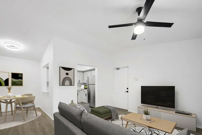 Living room, ceiling fan light fixture, hardwood style flooring, gray couch, flat screen TV, dining area with wooden table and chairs