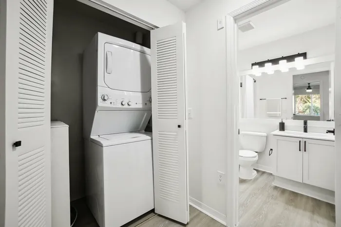 Laundry area with stacked washer and dyer, hardwood style flooring, bathroom with vanity lighting