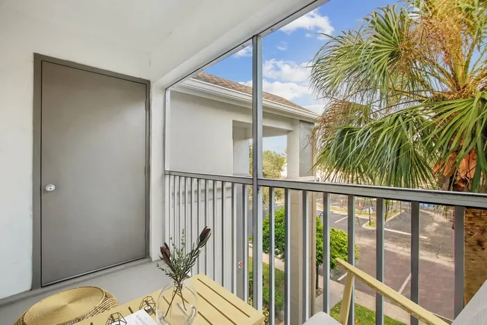 Screened in patio, gray storage door, palm trees and parking lot, wooden patio table