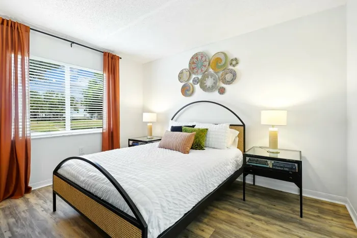 Bedroom, hardwood style flooring, black end table, twin bed with black framing, large window, circular wall art