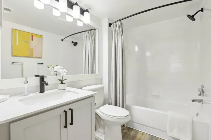 White quartz counters, shaker cabinets, vanity lighting and large mirror, toilet, bathtub, curved shower rod