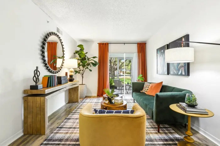 Living room, green velve couch, tan cushioned chair, rug on hardwood style flooring, round end table