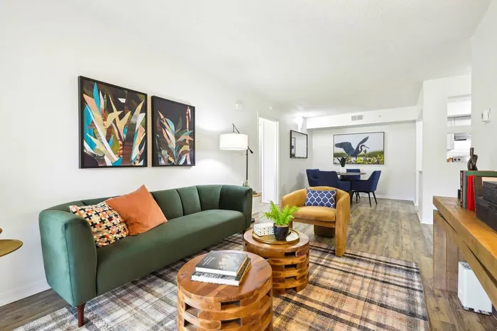 hardwood style flooring with rug, two circular coffee tables, green velvet couch, tan cushioned chair, wall art, standing lamp