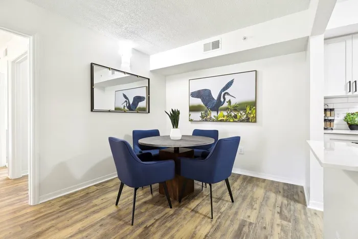 Dining area, round table, blue felt chairs, hardwood style flooring, bird wall art, rectangular mirror