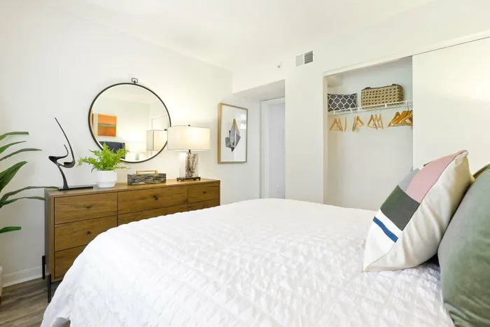 Bedroom, queen size bedding white bedding, sliding closet door, wooded table, circular mirror, table lamp
