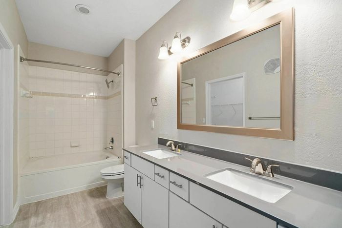 Bright and modern bathroom featuring dual sinks, elegant vanity, and a spacious bathtub with sleek fixtures.