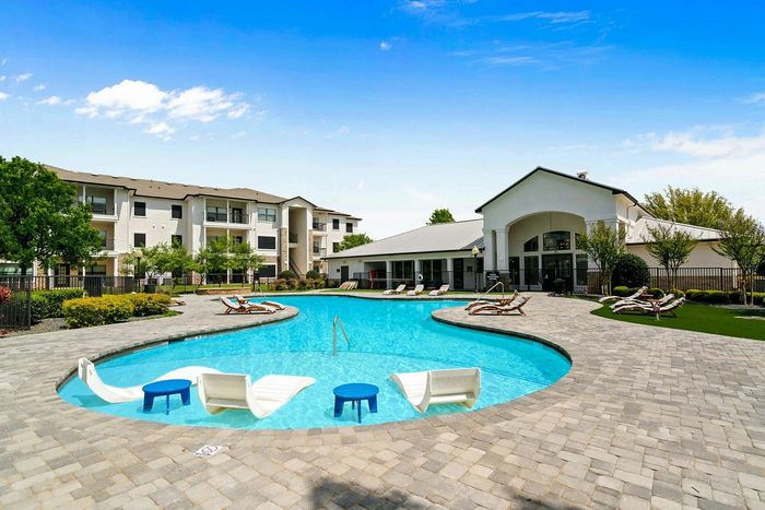 Inviting apartment complex featuring a stunning outdoor pool area with lounge chairs and beautiful landscaping under a clear blue sky.
