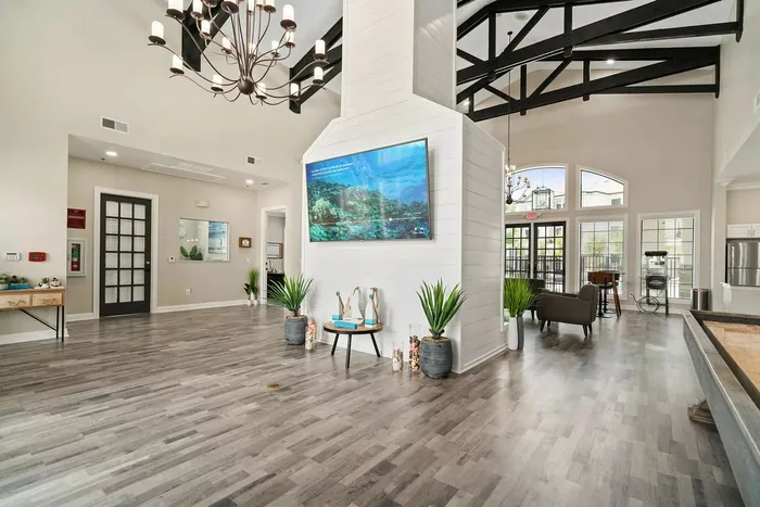 Elegant apartment lobby with high ceilings, modern chandelier, and stylish decor featuring a large screen and lush indoor plants.