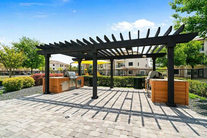 Inviting outdoor grilling area with modern pergola and lush landscaping in a vibrant community setting.