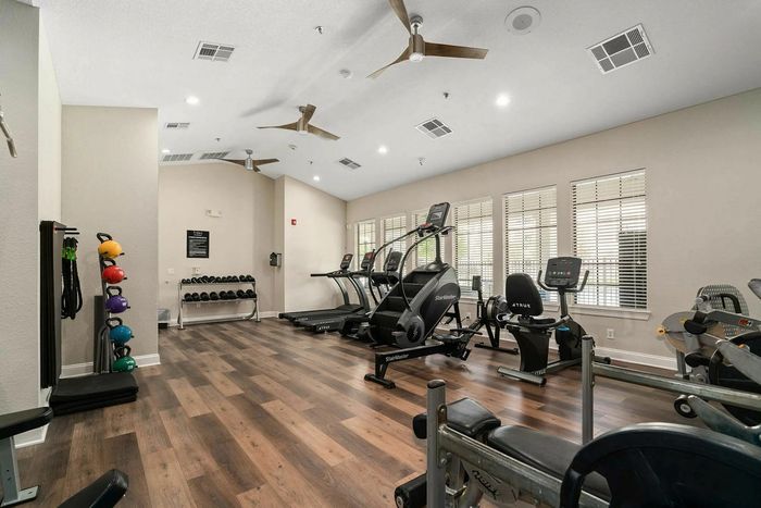 Modern fitness center with state-of-the-art equipment, including treadmills, stationary bikes, and colorful kettlebells, illuminated by natural light through large windows.