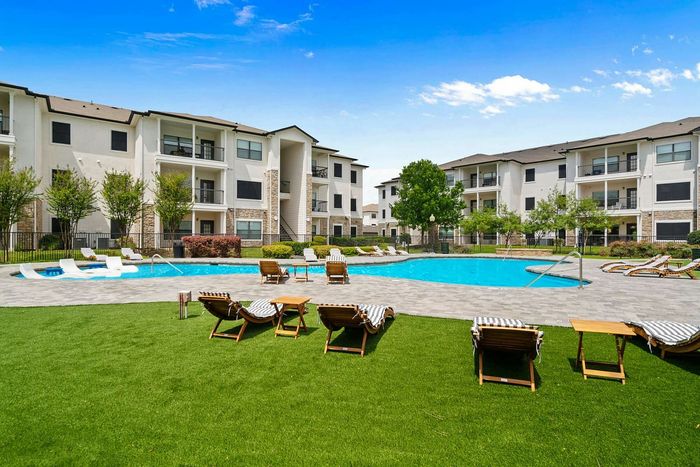 Elegant apartment complex with a stunning community swimming pool, lush green lawn, and comfortable lounging chairs for a relaxing ambiance.