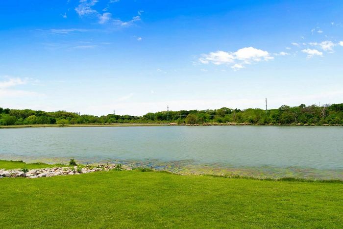 Serene lakeside view with lush greenery and a clear blue sky, offering a tranquil setting for relaxation and outdoor enjoyment.
