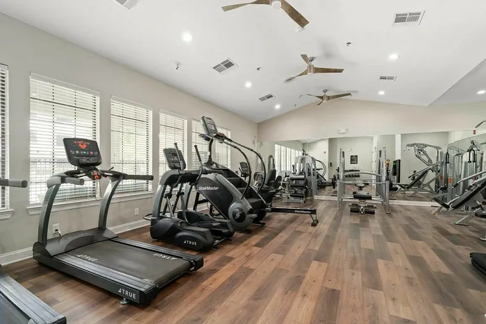 Modern apartment gym featuring state-of-the-art equipment, including treadmills and weight machines on stylish wood flooring.