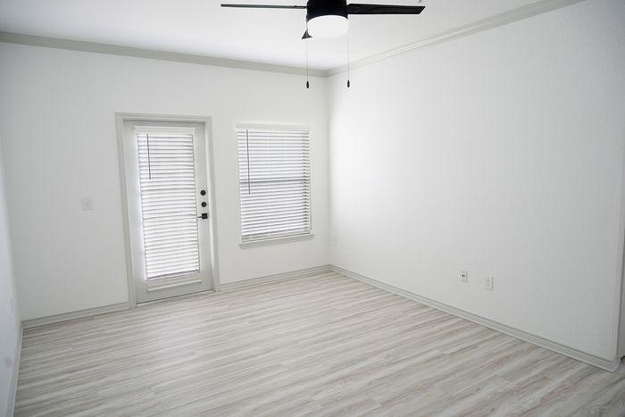 Bright and welcoming open living space with elegant hardwood flooring, modern ceiling fan, and ample natural light from large windows and patio access.
