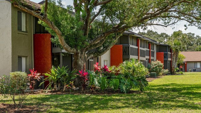 Charming apartment exterior with vibrant gardens, lush greenery, and inviting balconies in a serene setting.