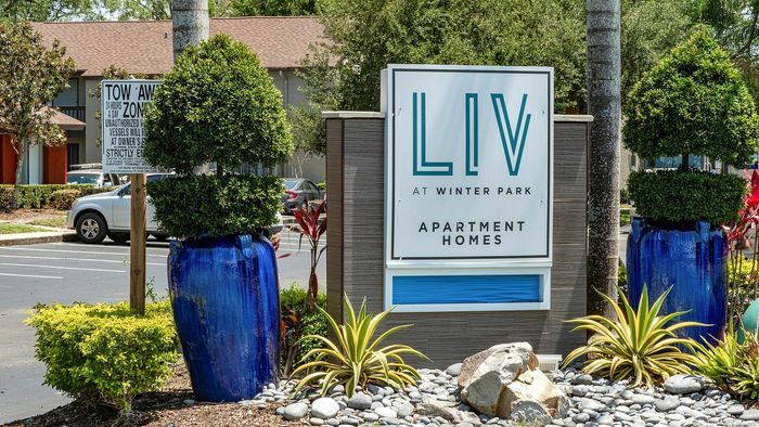 Inviting entrance to LIV at Winter Park Apartment Homes, featuring lush greenery and stylish blue planters in a serene setting.