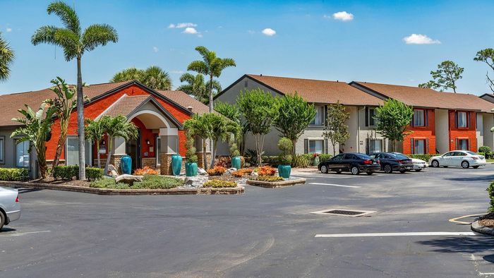 Charming apartment complex with vibrant landscaping, palm trees, and convenient parking under a clear blue sky.