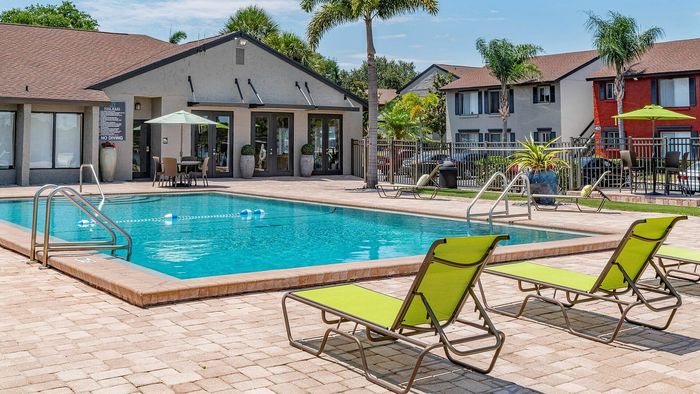 Inviting apartment community pool surrounded by lush greenery and modern lounge chairs, perfect for relaxation and leisure under sunny skies.